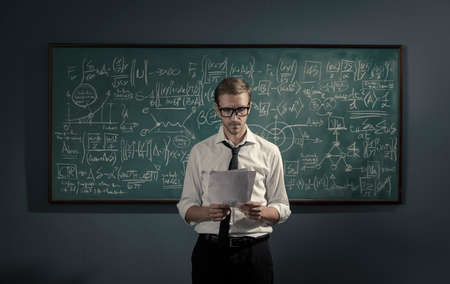 Confident young math professor standing in front of the chalkboard and explaining formulas,...