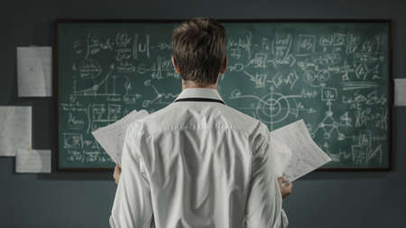 Young mathematician and researcher studying maths formulas on the chalkboard, back viewの写真素材