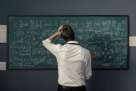 Young mathematician solving problems and writing formulas on the chalkboard, back view