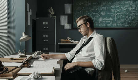 Young creative mathematician sitting at desk and working in the office, he is focused and studying a...