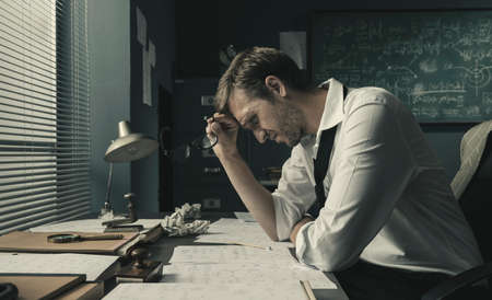 Math student sitting at desk and reviewing his papers, he is feeling confused and stressed