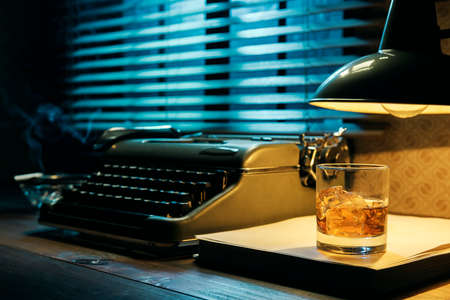 Vintage film noir style writer's desktop with typewriter and a glass of whiskey, creativity and inspiration conceptの写真素材
