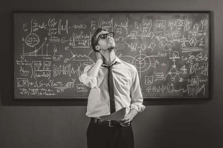 Math student standing in front of the chalkboard and feeling confused, he is not able to solve the...