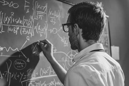 Young smart mathematician drawing math formulas on the chalkboard and thinking: he is solving problems and discovering new theoriesの写真素材