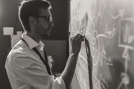 Young smart mathematician drawing math formulas on the chalkboard and thinking: he is solving...
