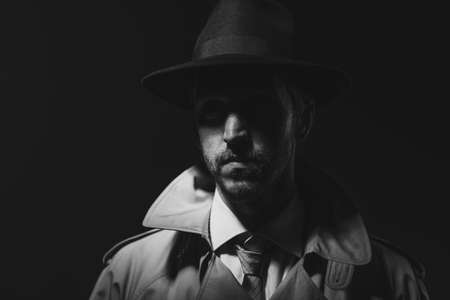 Noir film detective posing in the dark and staring at camera, thriller and crime conceptの写真素材