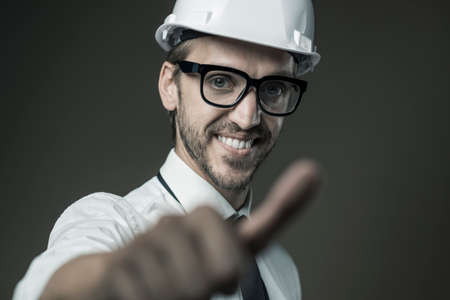 Smiling confident architect wearing a safety helmet and giving a thumbs upの写真素材