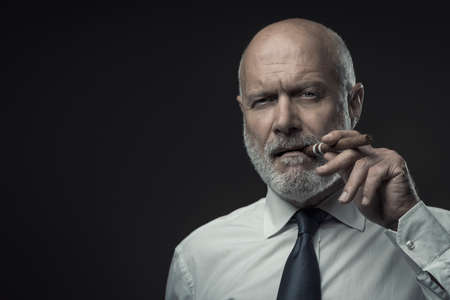 Confident senior business executive smoking a cigar and looking at cameraの写真素材
