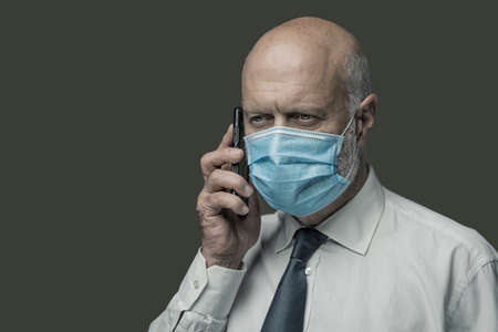 Corporate businessman wearing a face mask and talking on the phone, coronavirus prevention conceptの写真素材