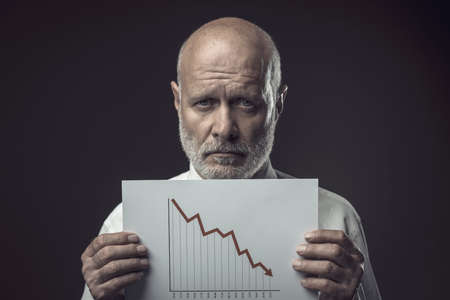 Worried businessman holding a negative financial chart, crisis and economical recession conceptの写真素材