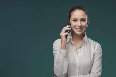 Young beautiful woman having a phone call with her smartphone, she is smiling at camera