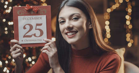 Happy woman showing a calendar on Christmas day and celebrating Christmas at home