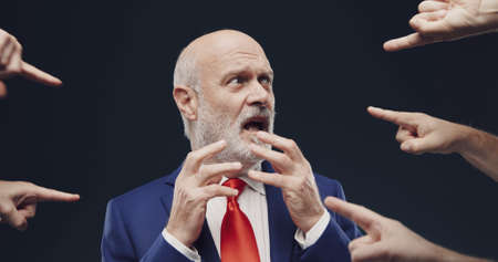 Many fingers pointing at one guilty businessman, he is scared and stressed
