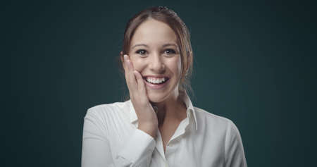 Surprised young woman smiling at camera, she is touching her face