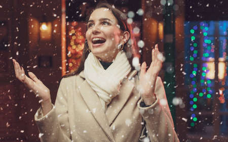 Happy woman walking in the street and watching snow falling at Christmasの写真素材