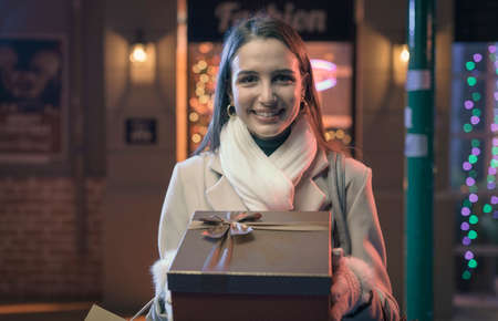 Happy woman doing Christmas shopping in the city street and holding a giftの写真素材