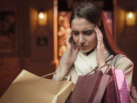 Stressed woman doing Christmas shopping in the city streets, she is having a bad headacheの写真素材