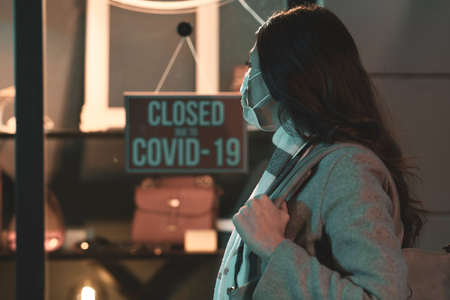 Store closed due to coronavirus covid-19 outbreak, a woman with surgical mask is reading the signの写真素材