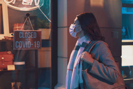 Store closed due to coronavirus covid-19 outbreak, a woman with surgical mask is reading the signの写真素材