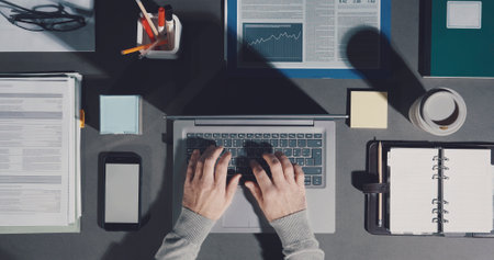 Corporate businessman working on a tidy organized desktop, he is typing on a laptop, top viewの写真素材