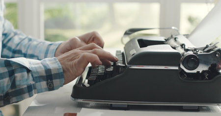 Man sitting at desk at home and typing on a vintage typewriter, creativity and storytelling concept