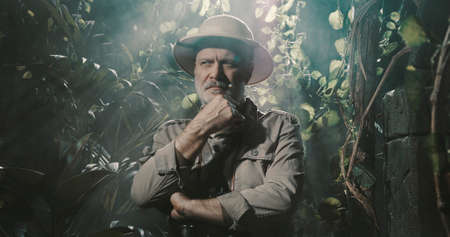 Brave explorer in the tropical jungle, he is thinking with hand on chinの写真素材