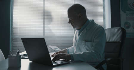 Professional doctor sitting at office desk and typing on his laptop, healthcare and technology conceptの写真素材