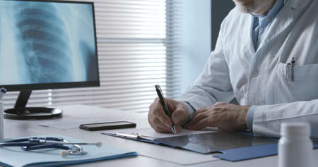 Professional doctor sitting at desk and writing a medical prescription for a patient