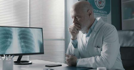 Professional doctor sitting at office desk and analyzing an x-ray image on the computer screen