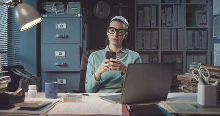 Inefficient office worker sitting at desk and chatting with her phone instead of working