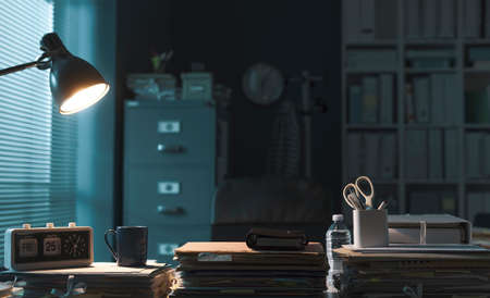 Corporate office interior with piles of paperwork and lit lamp, professional workspace conceptの写真素材