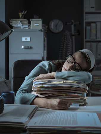 Exhausted office worker sleeping at desk and leaning on a pile of paperwork: overtime work and deadlines conceptの写真素材