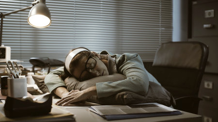 Exhausted young office worker sleeping at her desk, job burnout and overtime work conceptの写真素材