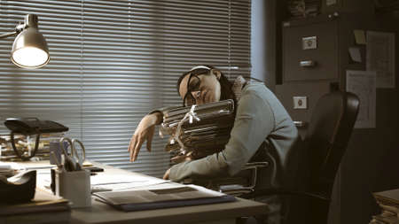Exhausted office worker sleeping at desk and leaning on a pile of paperwork: overtime work and deadlines conceptの写真素材