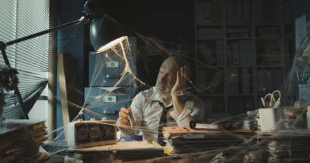 Corporate businessman dealing with business failure, he is sitting at desk in his dusty abandoned officeの写真素材