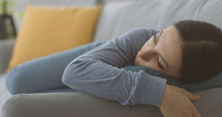 Depressed young woman lying down on the couch at home, stress and mental health concept