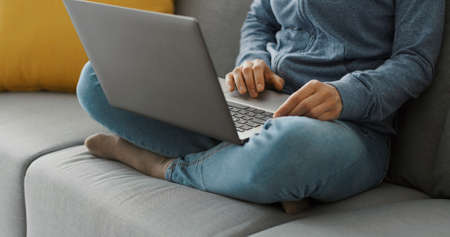 Woman sitting on the couch at home and connecting online with her laptop, remote work conceptの写真素材
