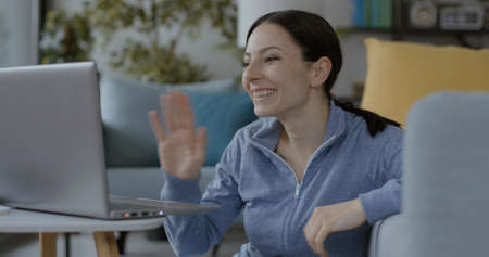 Cheerful woman video calling her friends on the laptop, she is waving and smiling