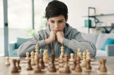 Young smart boy playing chess at home, he is focused and looking at the chessboard