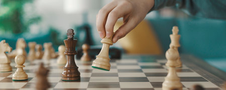 Intelligent boy playing chess at home, he is moving a piece on the chessboardの写真素材