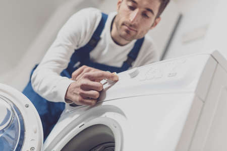 Repairman fixing a washing machine, he is adjusting a knob, professional service conceptの写真素材