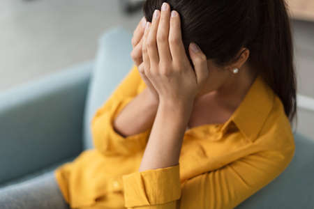 Young sad woman sitting in the living room, she is crying and covering her face