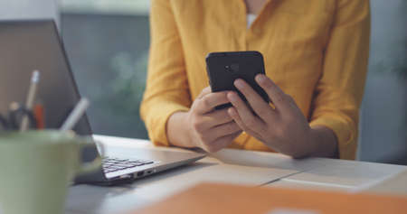 Woman sitting at desk in the office and sending messages with her smartphone