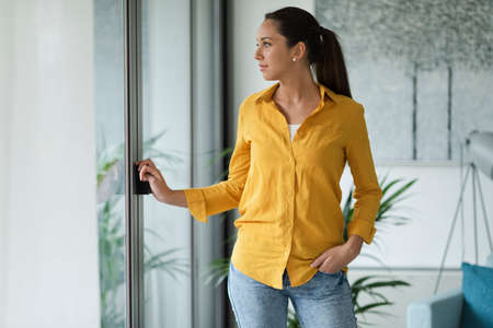 Young woman relaxing at home and looking outside the windowの写真素材