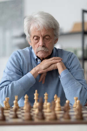 Elderly man playing chess, he is exercising his memory