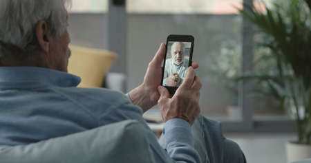 Elderly man video calling his online doctor from home, telemedicine conceptの写真素材