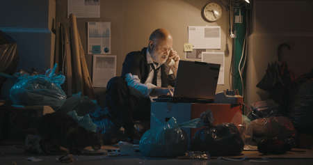 Homeless businessman sitting on the sidewalk and working with his laptop, financial crisis concept