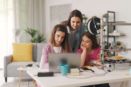 Smart girls learning 3D printing at home, their sister is helping them, education and science...