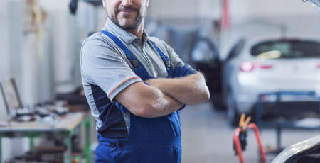 Mechanic posing in the auto repair shop, car service and assistance concept