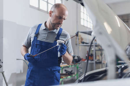 Professional mechanic doing a vehicle inspection, he is checking a car's oil level and quality using a dipstickの写真素材